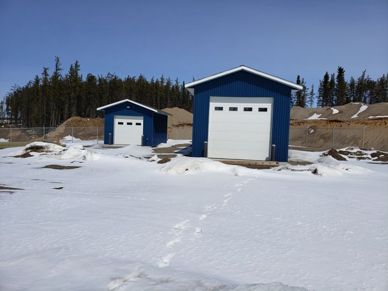 Two storage garages in the fenced yard, boreal forest behind